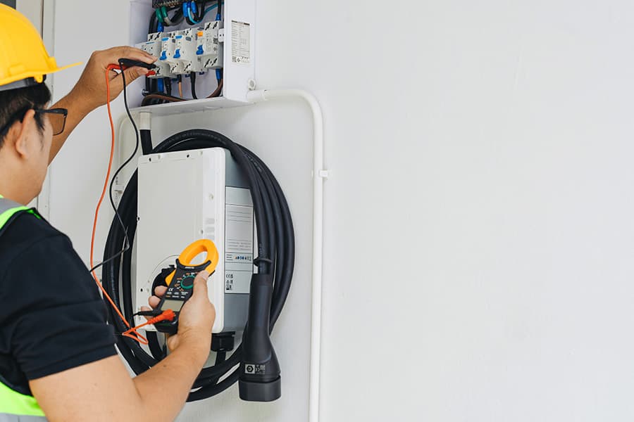 An engineer checking the electrical supply to an EV charger for repair.