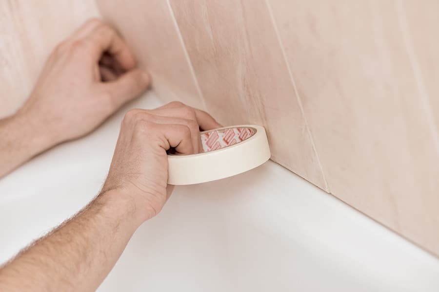 Masking tape being applied to the wall and the rim of a bath to prepare the area for new sealant.