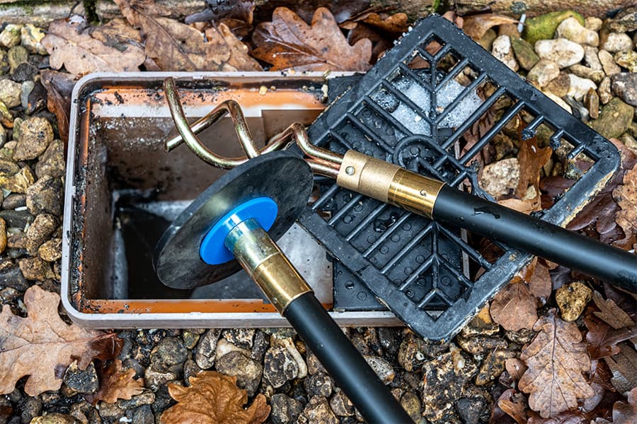 An outside drain being unblocked by a drain auger, a plumber's tool.
